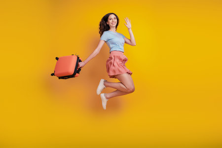 Full length photo of young attractive woman happy positive smile suitcase trip wave hello isolated...