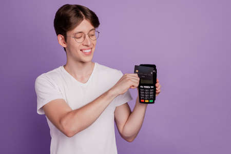 Photo of young cheerful guy payment bank card nfc atm cashless eyeglasses isolated on violet color backgroundの写真素材