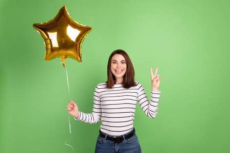 Photo of young lovely girl hold air balloons decoration show peace v-symbol isolated over green color backgroundの写真素材