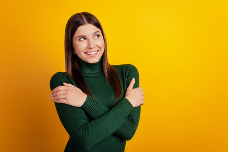 Photo of dreamy inspired lady hug herself look empty space dream wear green shirt isolated on yellow...