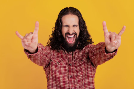 Photo of crazy harsh rocker man show horns enjoy concert wear checkered shirt isolated on yellow...