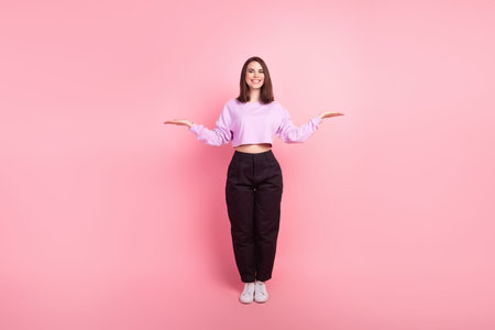 Full length photo of young cheerful girl hold hands advertise proposition isolated over pink color...