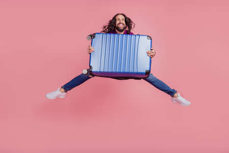 Full body photo of young cheerful guy jump air hold baggage journey isolated on pink color backgroundの写真素材