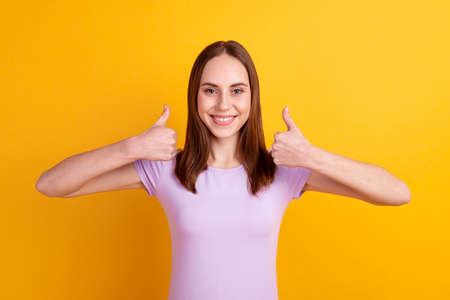Photo of young lovely woman show thumb-up approve quality promotion isolated over yellow color backgroundの写真素材