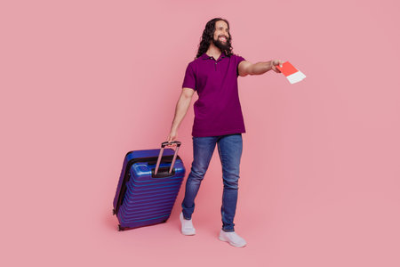 Photo of man hold tickets walk carry luggage airport check-in wear purple t-shirt isolated on pink color backgroundの写真素材