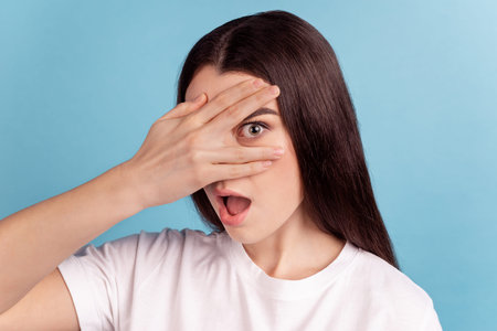 Photo of young girl astonished cover eye arm look horror film fear scared nervous isolated over blue...