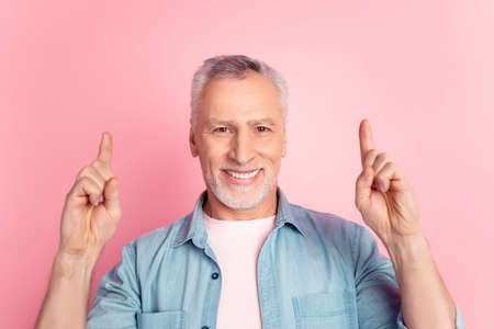 Photo of cheerful aged man indicate fingers empty space ad choice suggest discount isolated over pink color backgroundの写真素材