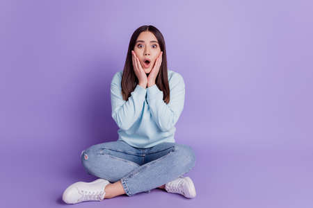 Photo of shocked funny lady sit floor hands cheeks open mouth wear blue shirt isolated on purple backgroundの写真素材