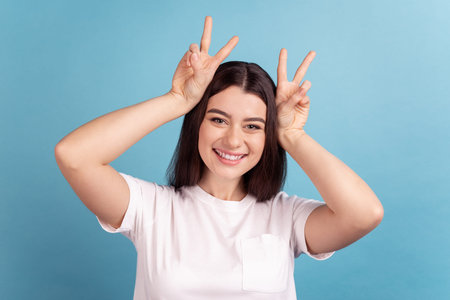 Photo of young pretty girl have fun show fingers pet ears playful grimacing isolated over blue color...
