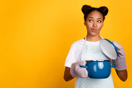 Photo of young african girl housewife wondered dreamy look empty space cooker isolated over yellow color backgroundの写真素材