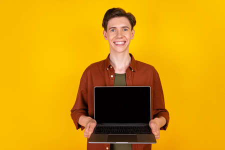 Photo of young cheerful man show laptop promo offer proposition manager isolated over yellow color backgroundの写真素材