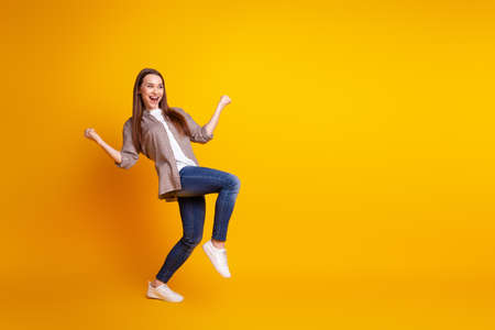 Full length profile side photo of young lovely woman rejoice victory fists hands look empty space isolated over yellow color backgroundの写真素材