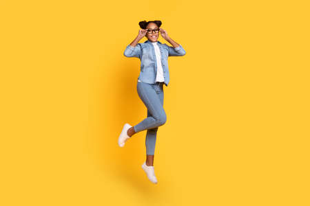 Full size profile side photo of young cheerful african lady jump eyewear energetic isolated over yellow color backgroundの写真素材
