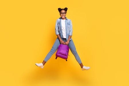 Full length photo of young african girl have fun jump up energetic hold backpack isolated over...