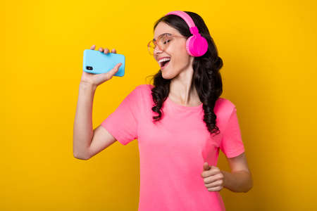 Photo of young excited girl have fun listen music headphones sing karaoke star isolated over yellow color backgroundの写真素材