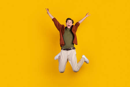 Full length photo of young man astonished jump up scream wear casual clothes isolated over yellow color backgroundの写真素材