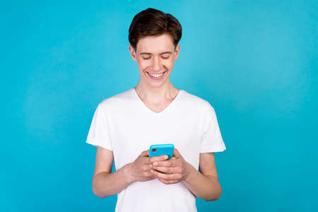 Photo of young cheerful man use smartphone button app download influencer isolated over blue color backgroundの写真素材