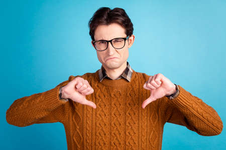 Photo of young guy show thumbs-down dislike displeased bad spoiled ad isolated over blue color backgroundの写真素材