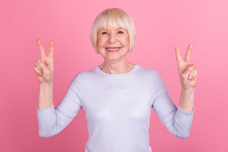 Photo of senior woman good mood show fingers peace cool v-symbol travel isolated over pink color...