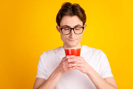 Photo of young handsome guy enjoy morning latte americano cup break isolated over yellow color backgroundの写真素材