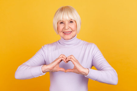 Photo of cheerful pretty woman show fingers heart symbol love feelings isolated over yellow color...