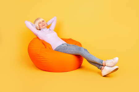 Full body profile side photo of senior woman rest enjoy weekend chair isolated over yellow color backgroundの写真素材