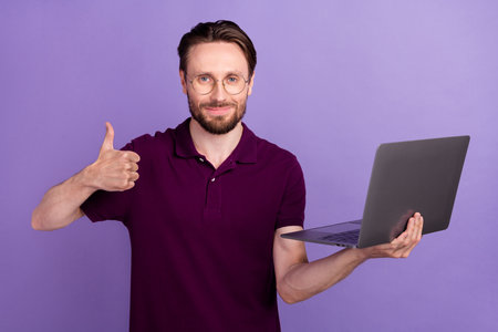 Photo of young man use laptop show figner thumb-up approve good ideal isolated over violet color backgroundの写真素材