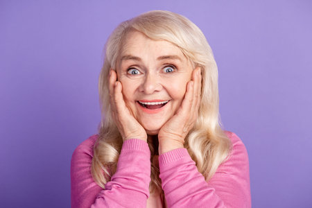 Photo of aged excited cheerful woman hands touch cheeks reaction isolated over purple color...