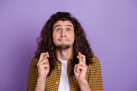 Photo of young man look empty space crossed fingers pray wish luck isolated over purple color...