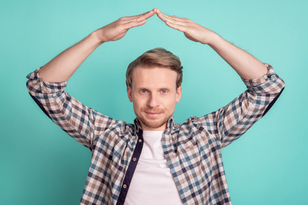 Photo of real estate agent man hold hands above head suggest buy house wear plaid shirt on teal color backgroundの写真素材