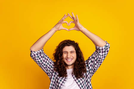 Photo of young cheerful man show fingers heart symbol love feelings romantic isolated over yellow color backgroundの写真素材