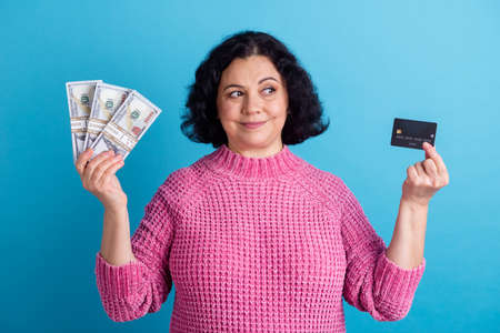 Photo of elderly woman happy positive smile hold cash money dollars credit card isolated over blue color backgroundの写真素材