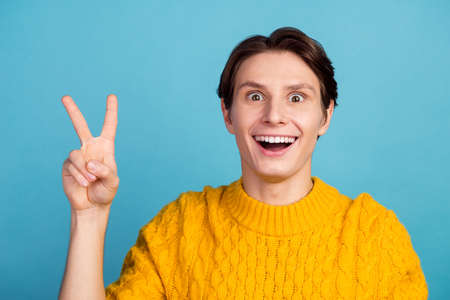 Photo of young man happy positive smile show peace v-sign isolated over blue pastel color backgroundの写真素材