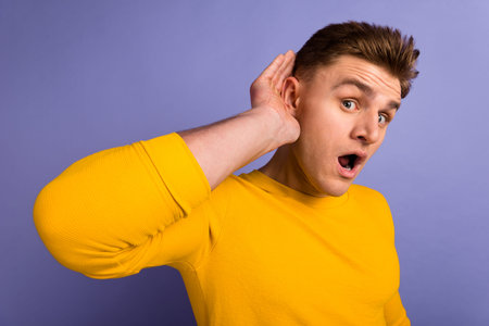 Photo of young impressed guy hand near ear listen rumor secret reaction isolated over violet color...