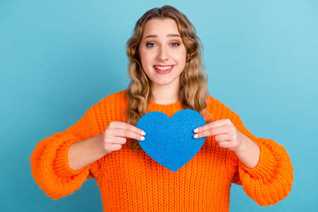 Photo of cheerful nice happy young woman hold hands blue heart paper shape isolated on blue color backgroundの写真素材