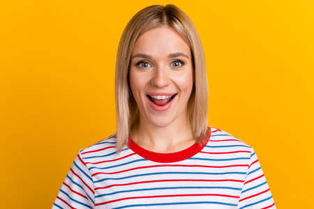 Close-up portrait of young pretty surprised woman with opened mouth standing isolated on yellow color backgroundの写真素材