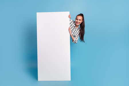 Cheerful female hiding near big cellphone blank screen advertising application over blue studio backgroundの写真素材