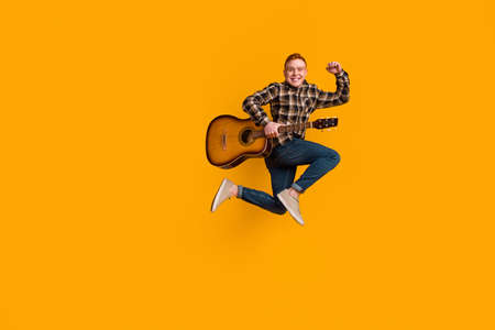 Full length photo of young guy jumper active celebrate luck fists hand play guitar concert isolated over yellow color backgroundの写真素材
