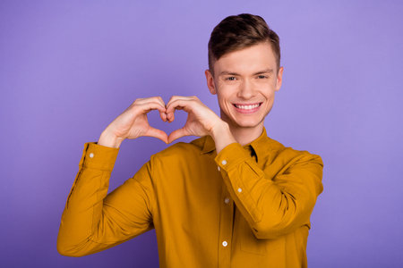 Photo of young guy boyfriend show fingers heart shape romantic feelings isolated over violet color backgroundの写真素材