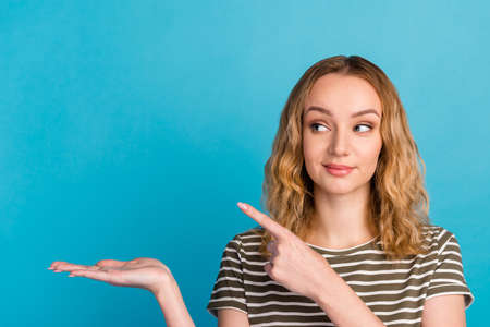 Smiling young lady holding hand with open palm advertising showing free empty space poiting isolated on blue studio wallの写真素材