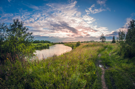 beautiful landscape of the riverbank at sunset with the sun above the horizonの写真素材