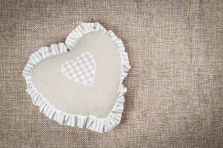 Beige heart-shaped pillow for home against the background of burlap sofaの写真素材