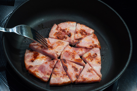 slices of fried ham in a frying pan, laid out in the form of a heart with a fork close-up, breakfast for loversの写真素材