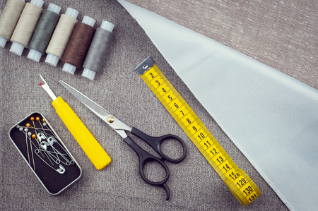 sewing pattern, composition with scissors, spools of thread, pins, measuring tape, Seam ripper, background of gray fabrics, top viewの写真素材