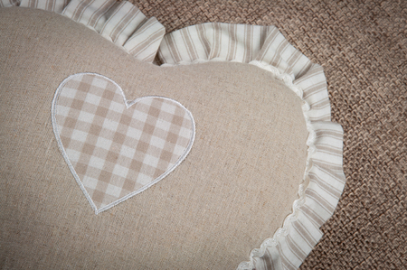 Beige heart-shaped pillow for home against the background of burlap sofa, close-upの写真素材