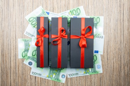 Three black matte gift box with a bow with euro banknotes on a wooden table. top viewの写真素材