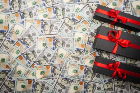Three black matte gift boxes with a bow on the background of dollars banknotes. top view, copy spaceの写真素材