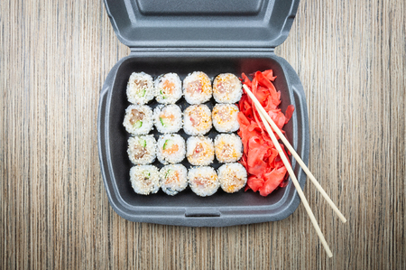 Sushi rolls in a plastic container on a wooden table. top viewの写真素材