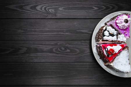 Different pieces of cake in a plate on a dark wood background. top viewの写真素材