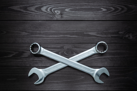 The crosshair of two chrome wrenches on a dark wooden workbench.の写真素材
